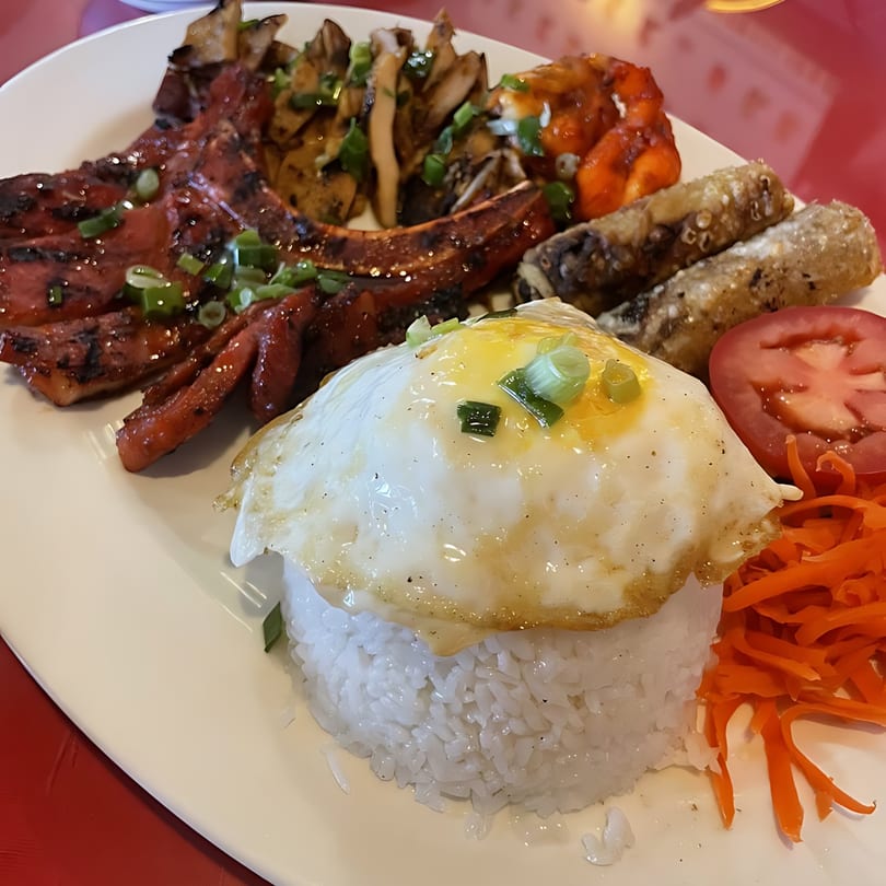 Vietnamese grilled pork chop, shrimp, egg rolls, fried egg, rice, and pickled carrots.