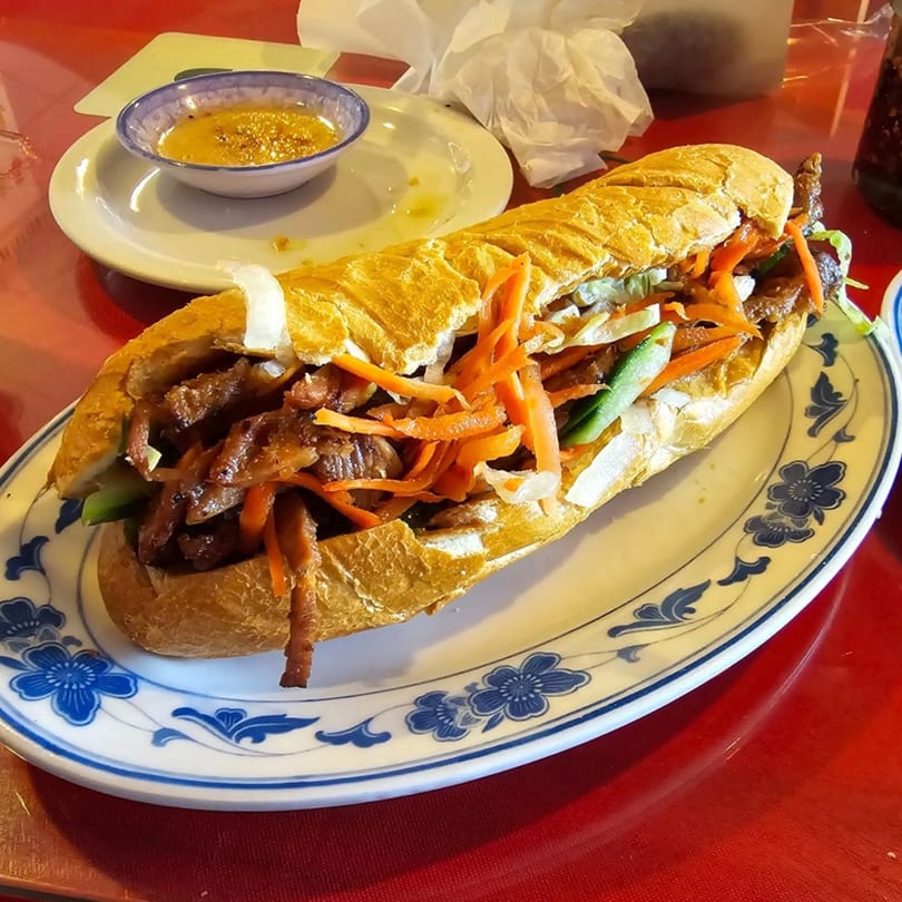 A Vietnamese banh mi sandwich with grilled meat and pickled vegetables on a decorative plate.