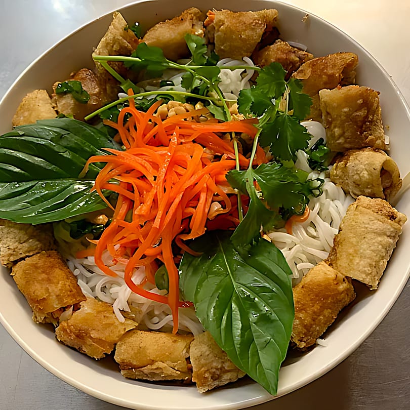 A Vietnamese vermicelli bowl with crispy spring rolls, shredded carrots, peanuts, and fresh herbs.