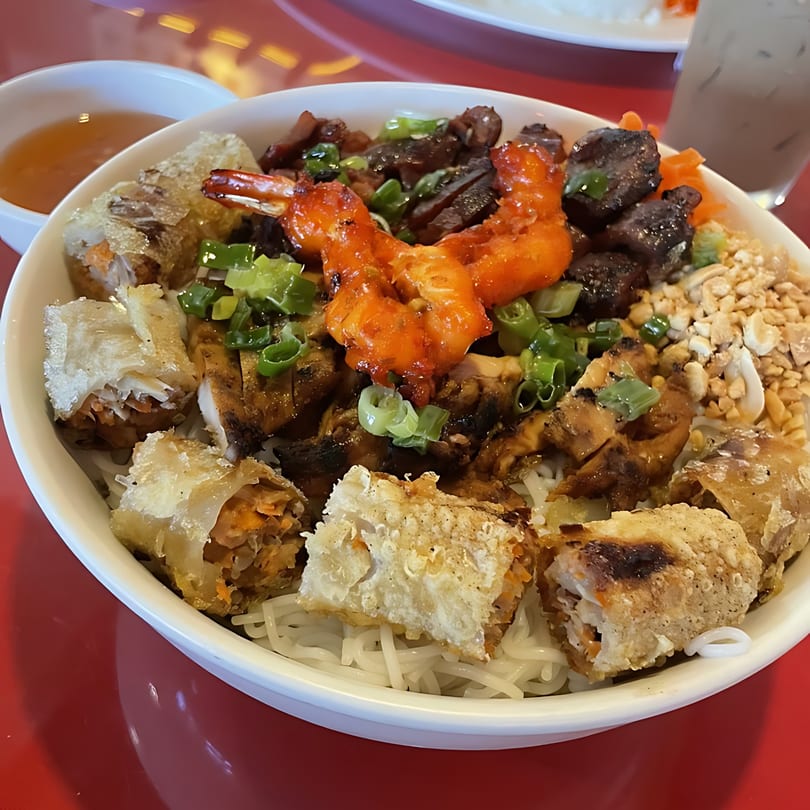 A Vietnamese vermicelli bowl with grilled shrimp, beef, chicken, spring rolls, and peanuts.