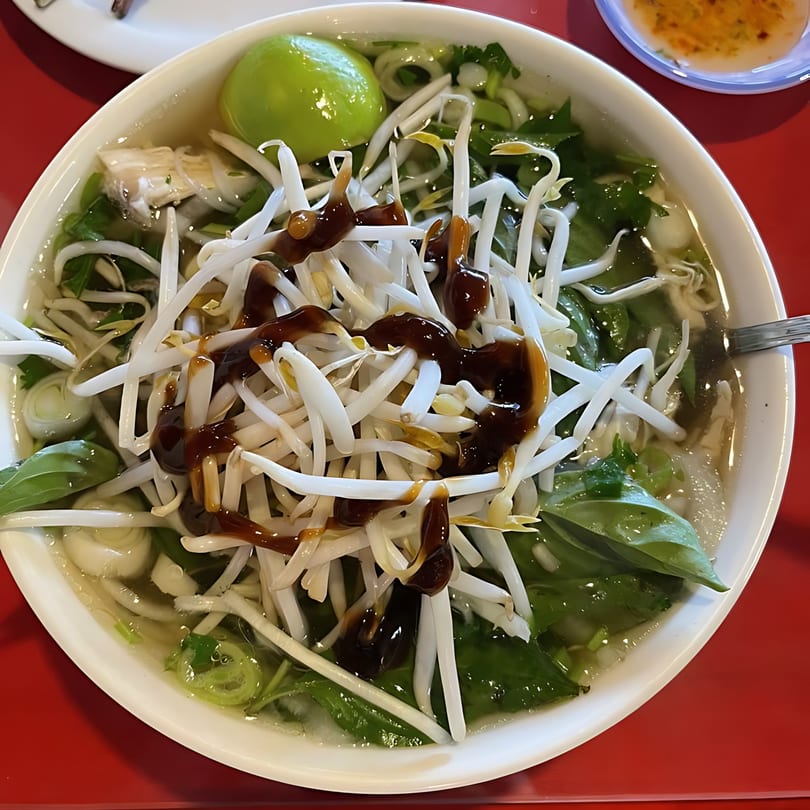 A close-up of a bowl of Vietnamese pho, topped with bean sprouts, lime, and sauce.
